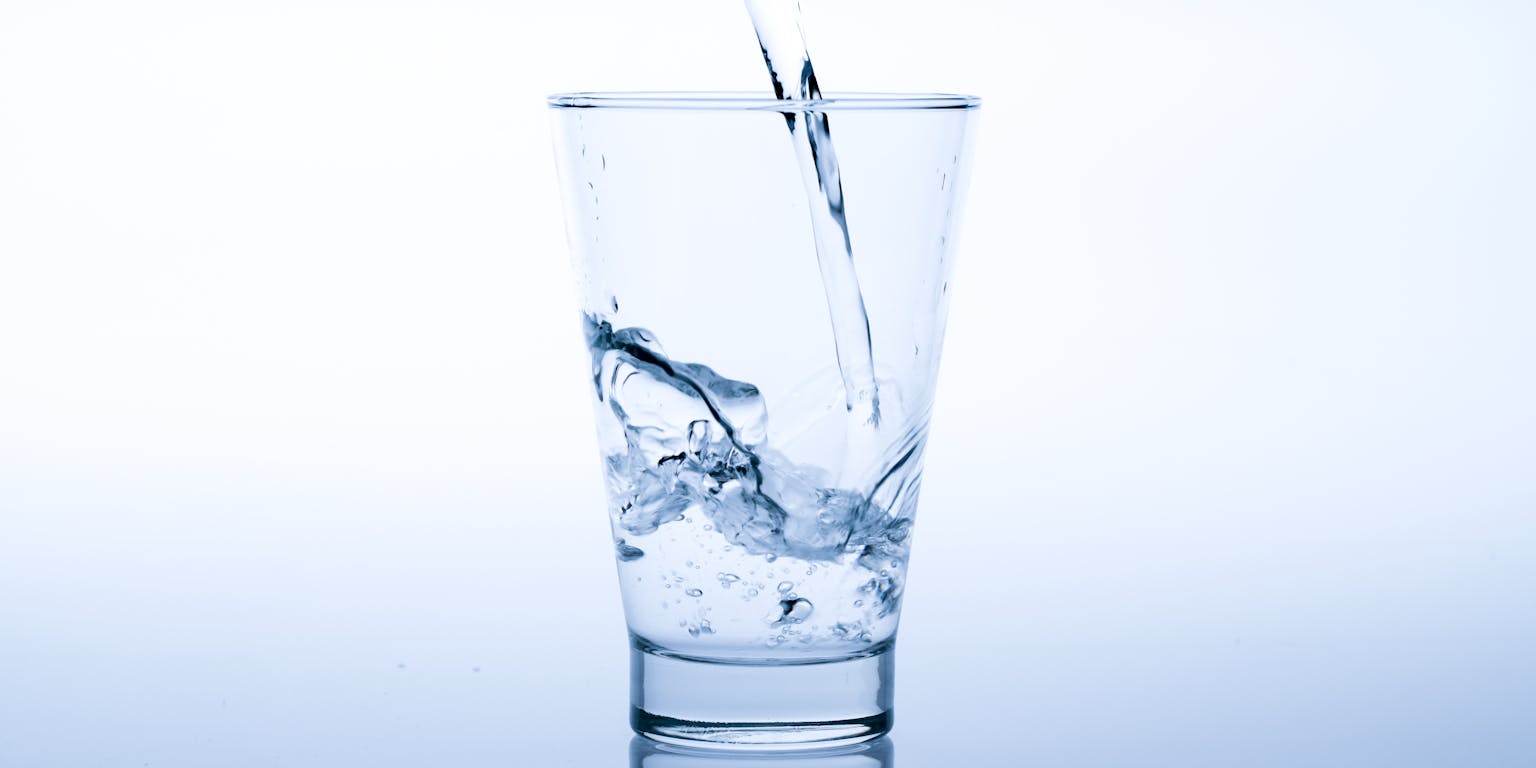 Close-up van een glas waar water in wordt geschonken.