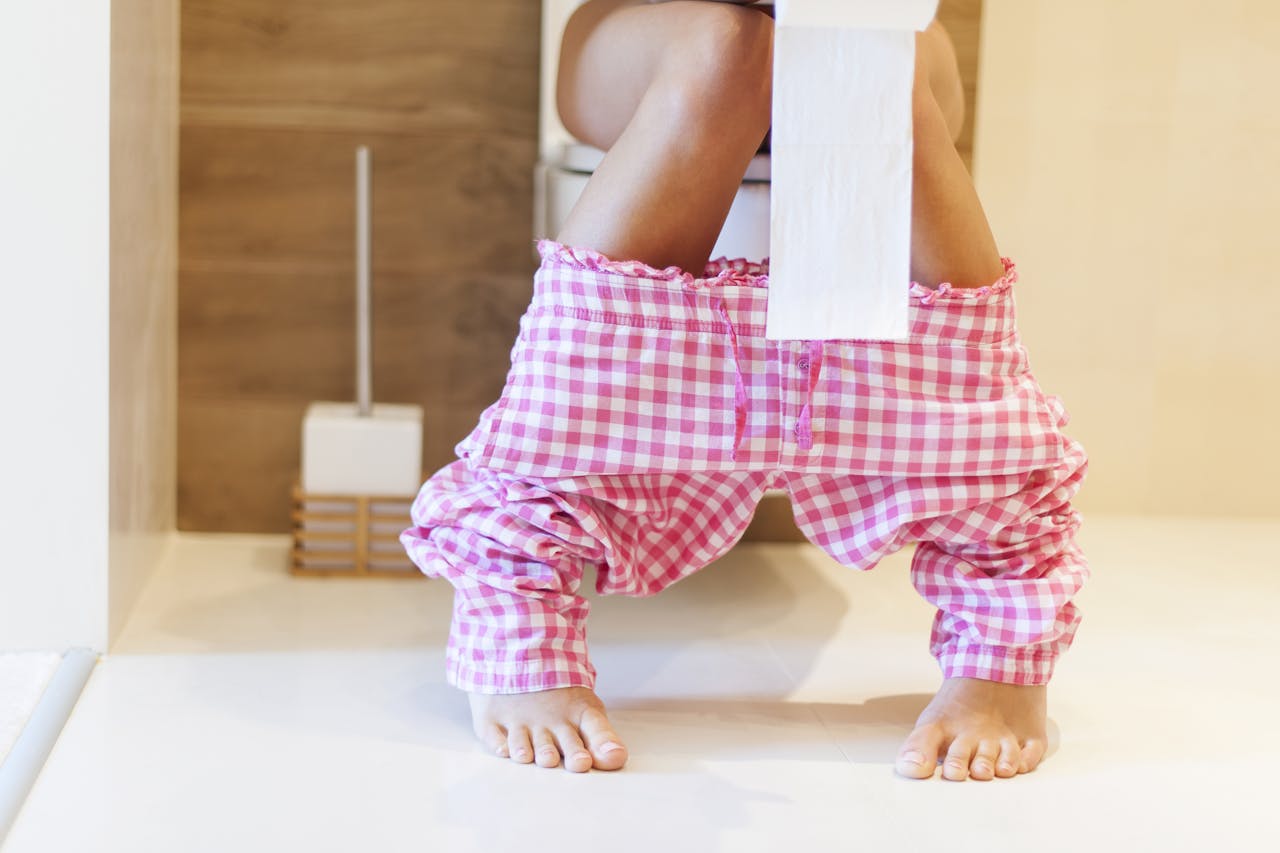 Wat doen bacteriën écht in onze darmen? vrouw met geblokte broek zit op de wc en houdt een toiletrol vast