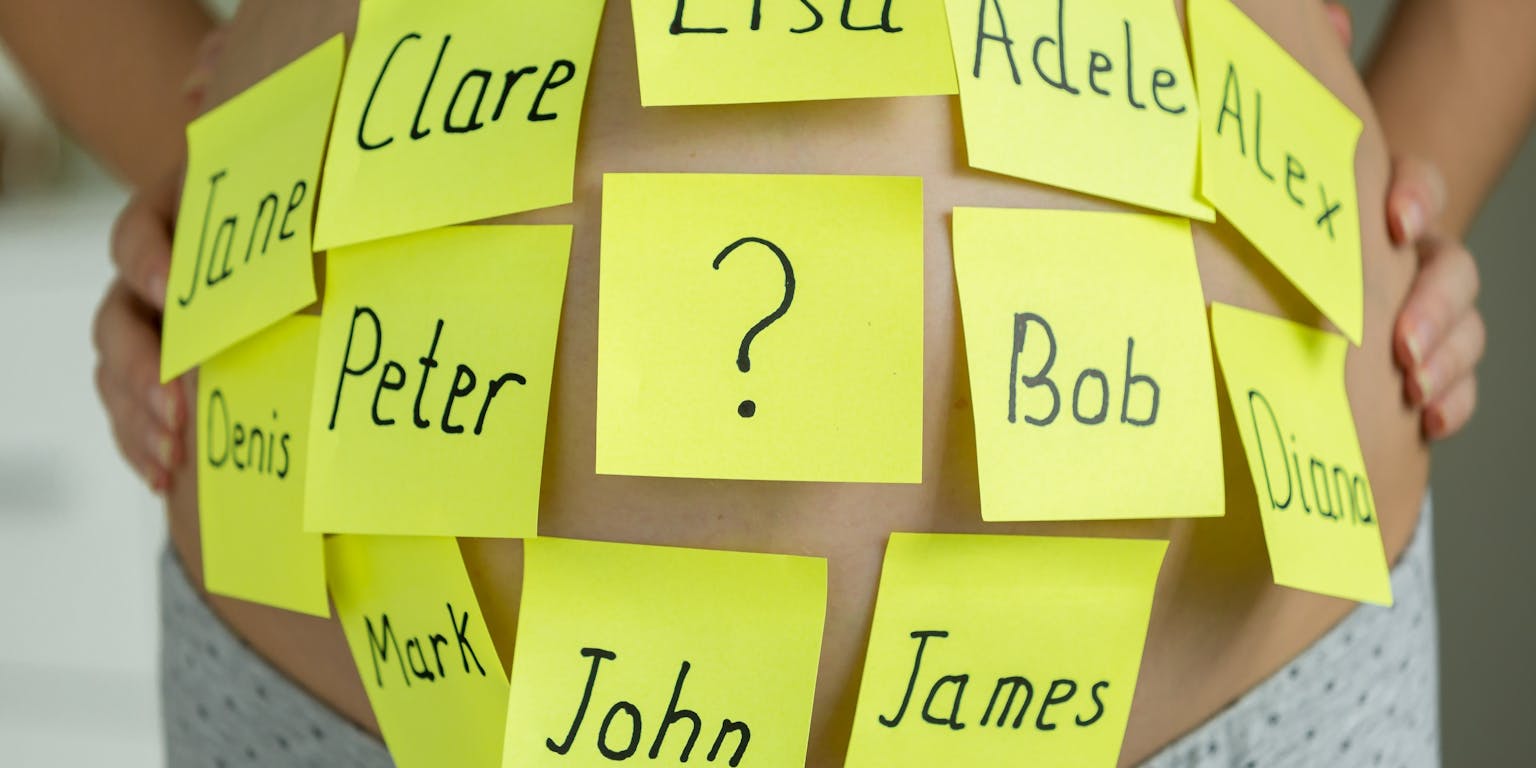 De buik van een zwangere vrouw met plakbriefjes erop. Op de briefjes staan verschillende namen.