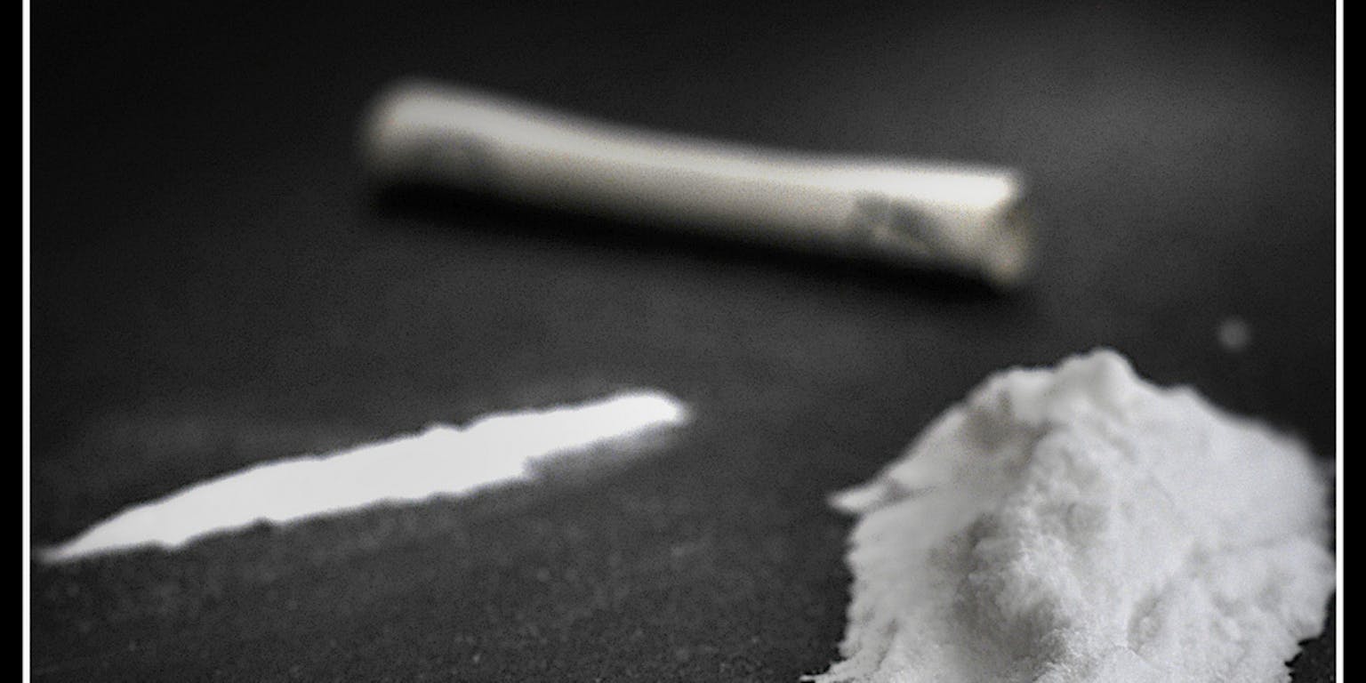 Een hoopje cocaïne, een lijn cocaïne en een opgerold biljet op een zwarte ondergrond.