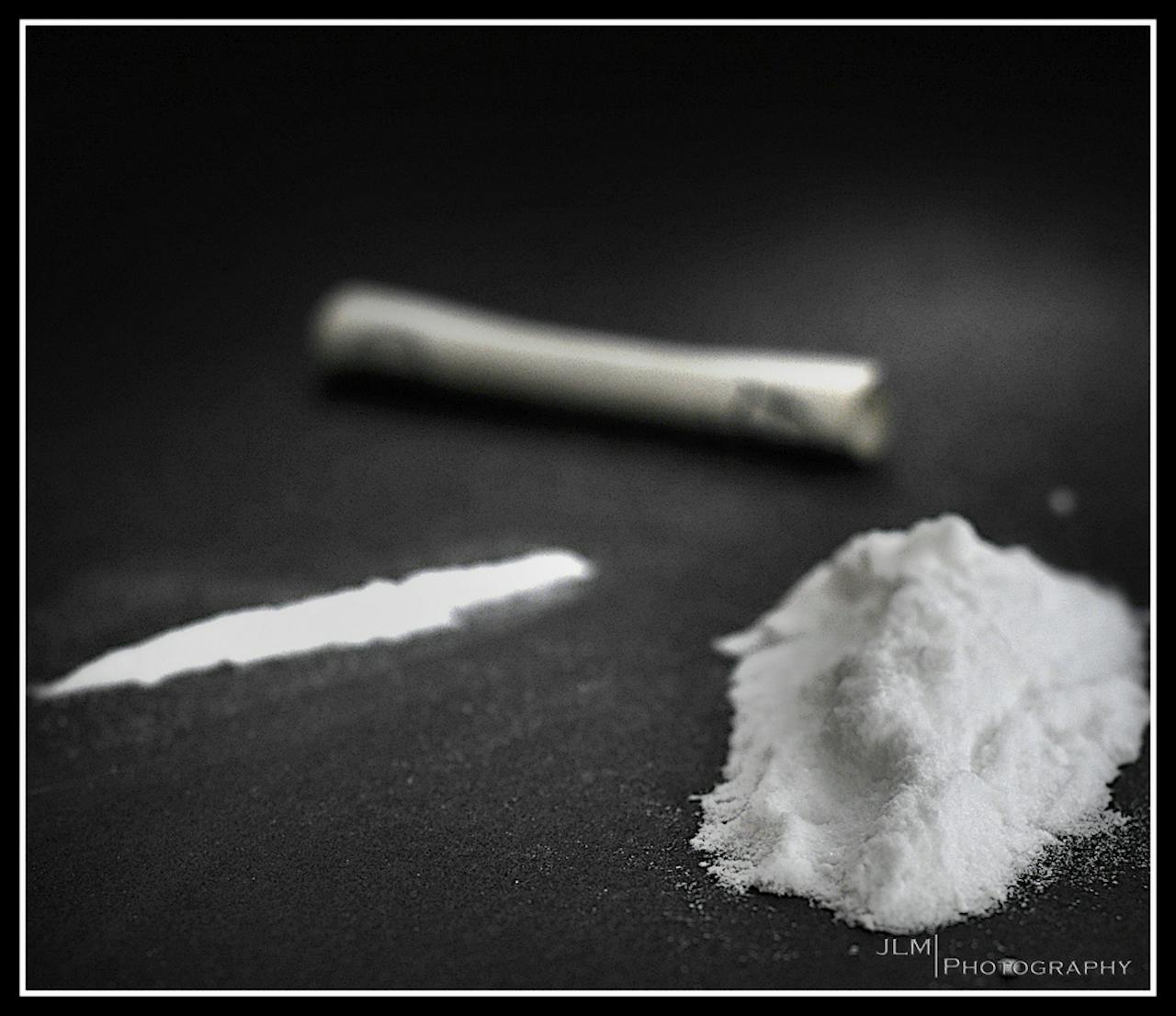 Cocaïne. Een hoopje cocaïne, een lijn cocaïne en een opgerold biljet op een zwarte ondergrond.