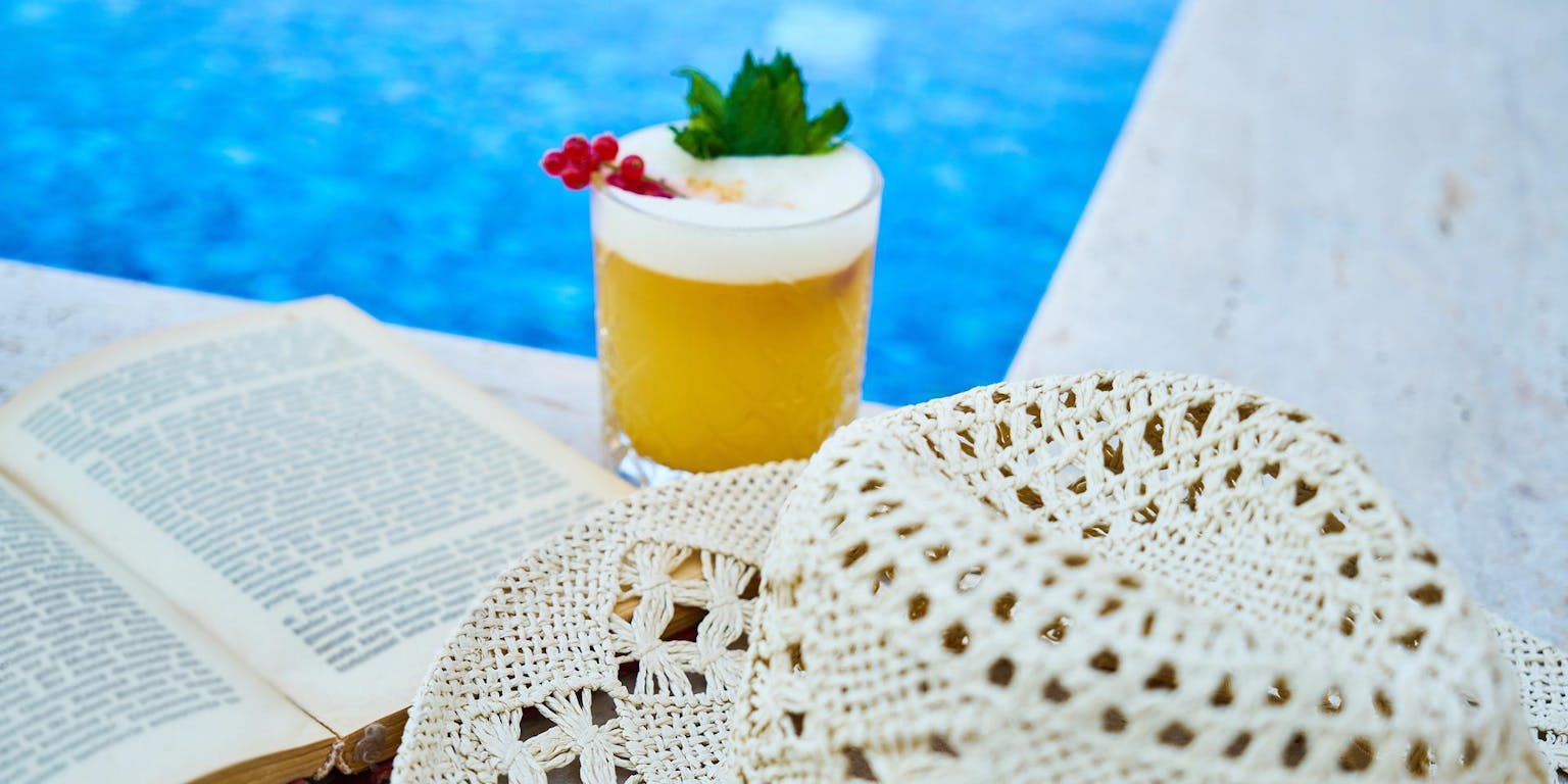 Een hoed, een drankje en een boek naast het zwembad.