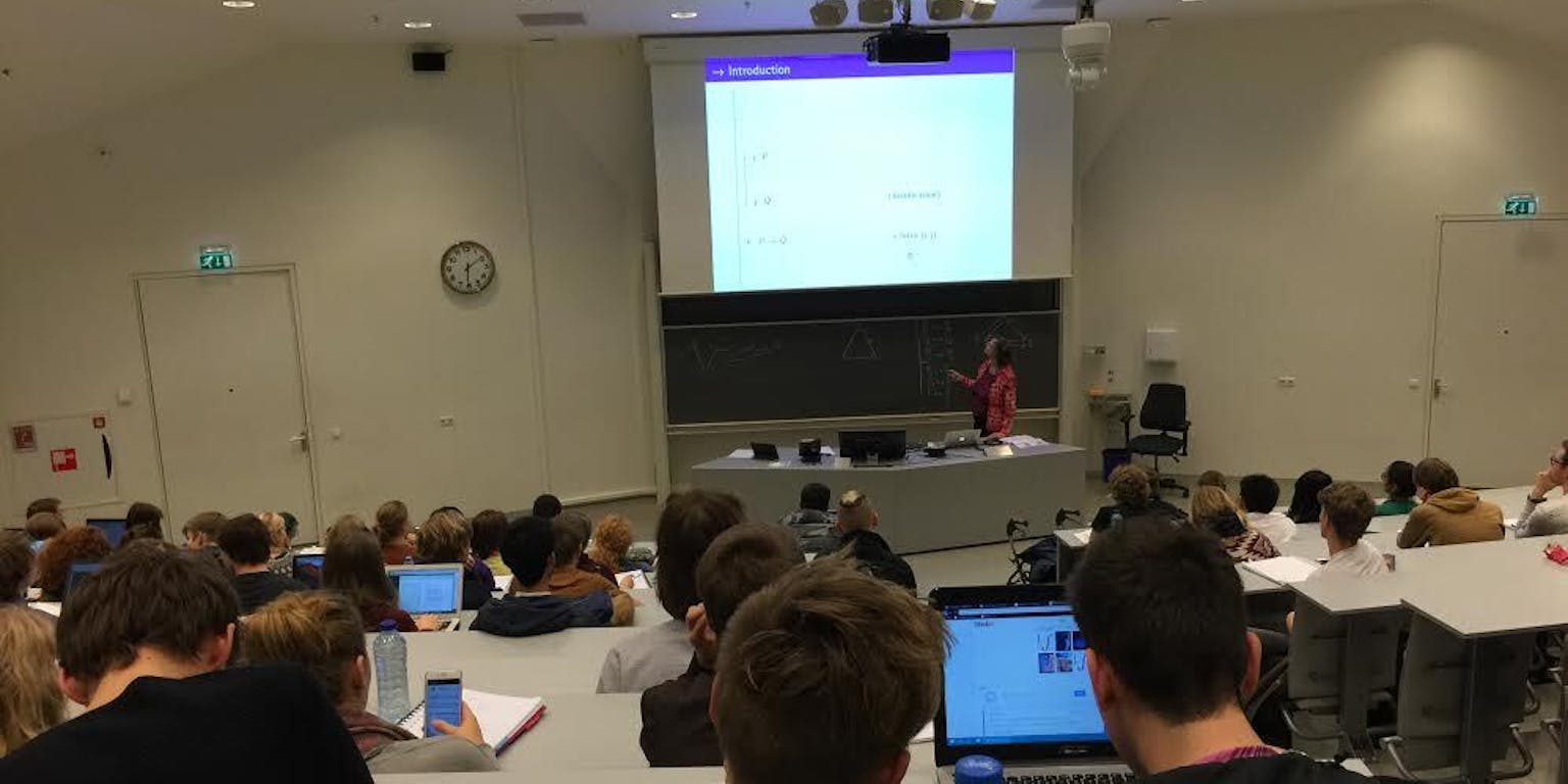 Een collegezaal met veel mensen die aan bureaus zitten.