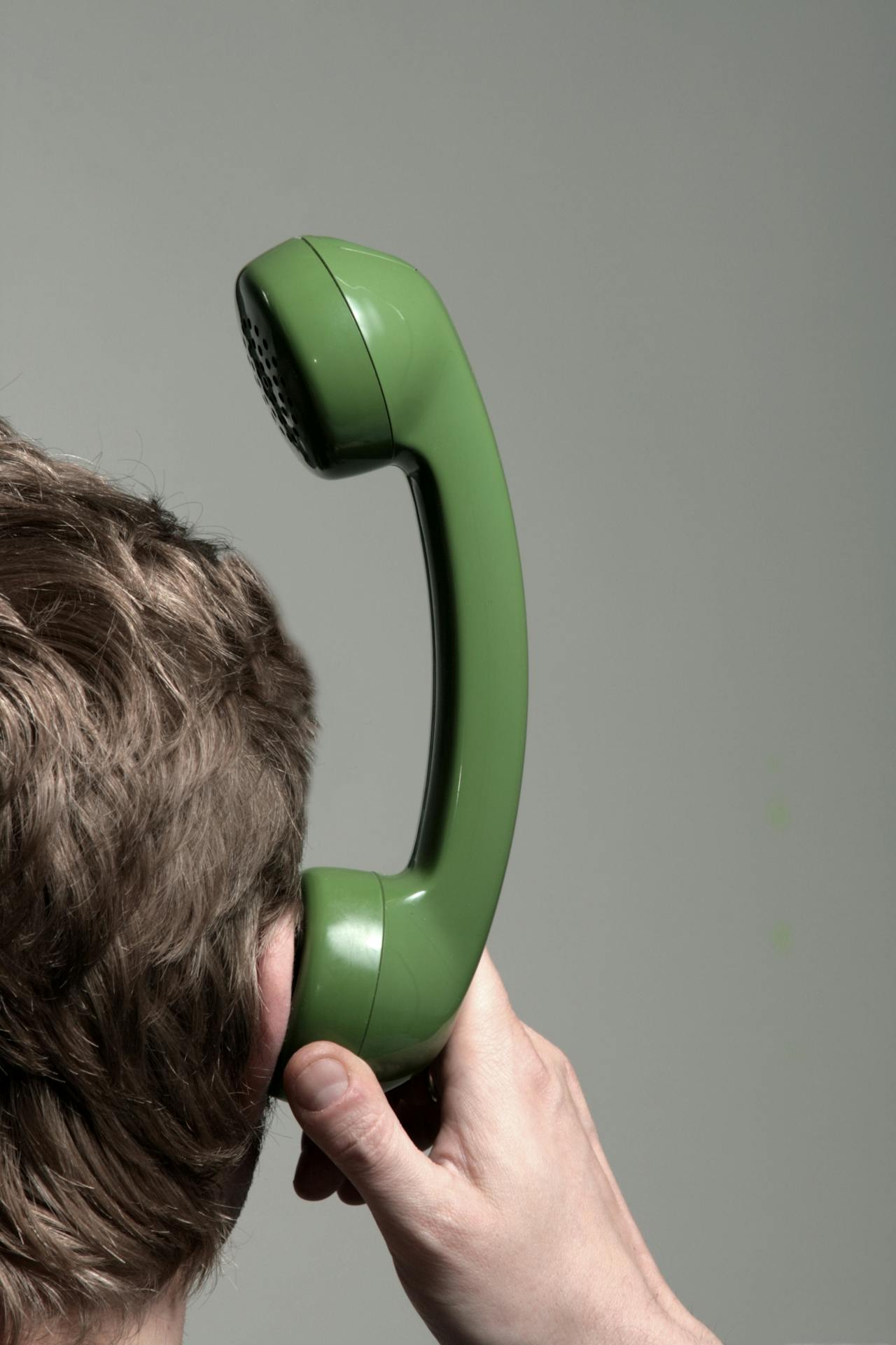 Mens met groene telefoonhoorn tegen diens oor.