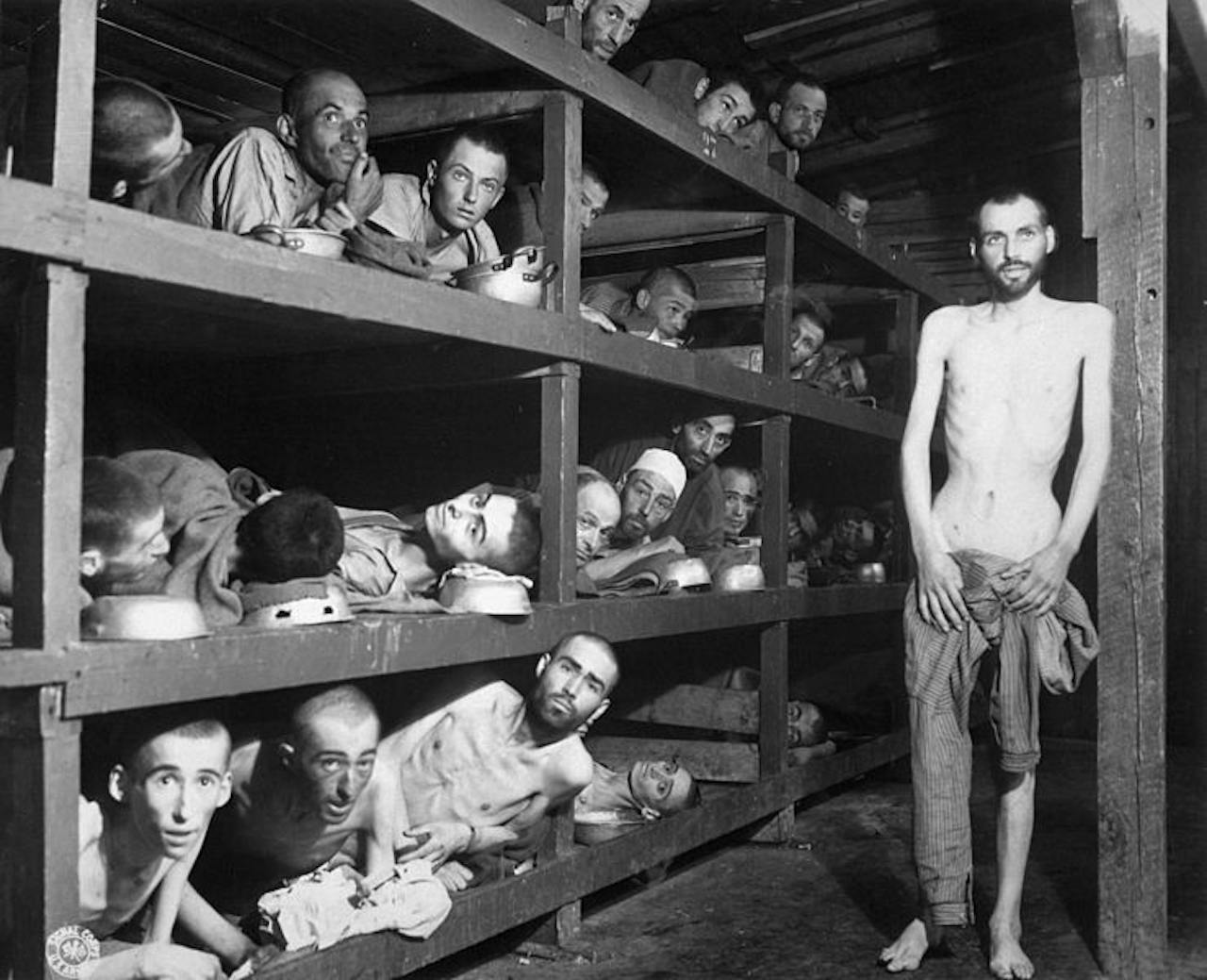 Een oude zwart-witfoto van een groep mannen liggend in een barak in een concentratiekamp.