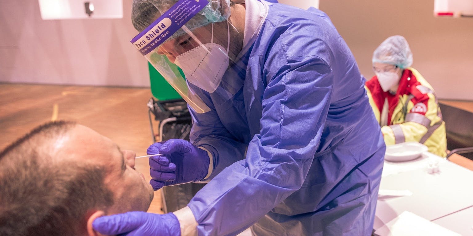 Een persoon in beschermende kleding neemt een coronatest af bij een persoon.