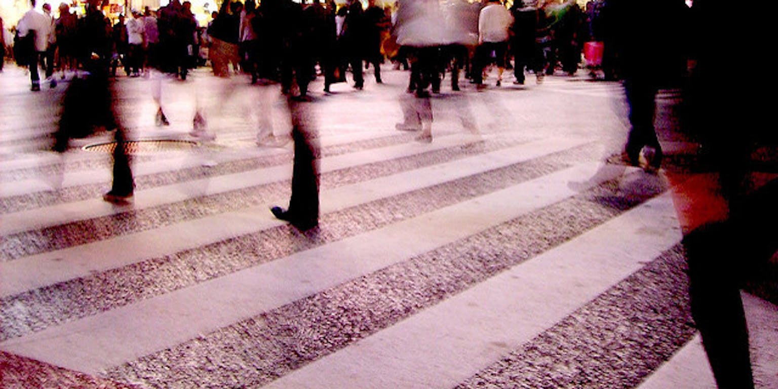 Een groep mensen kruist elkaar op een zebrapad in het donker.