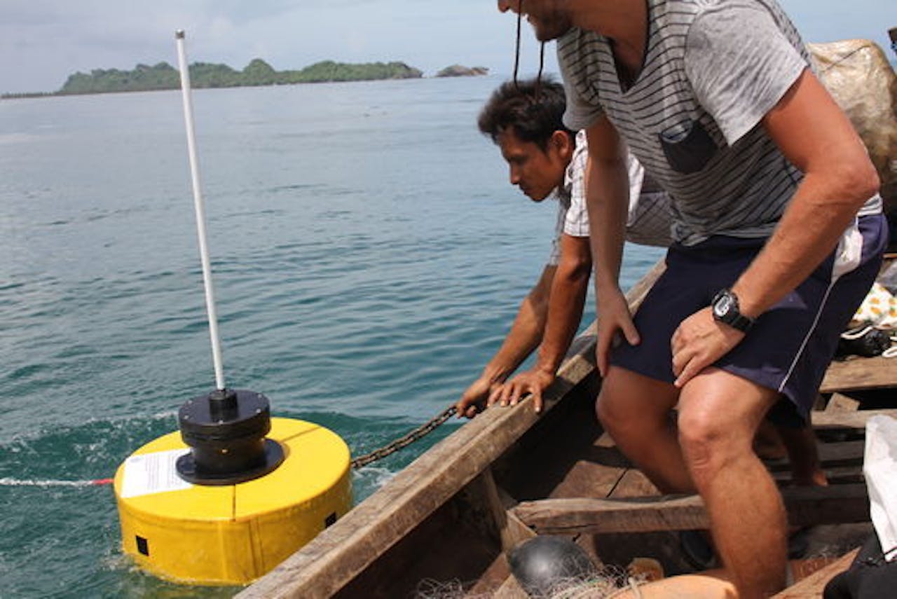 Twee mannen op een boot kijken naar een gele boei. Met deze slimme boei, de zogeheten Wavedroid, wordt onder meer de golfhoogte gemeten.