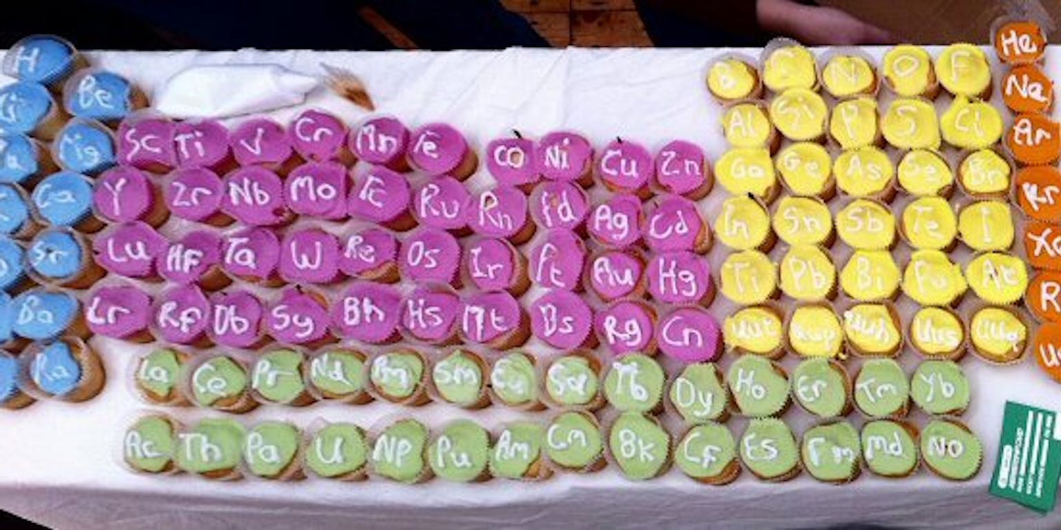 Een tafel vol met paarse, groene en gele cupcakes met elementen erop.