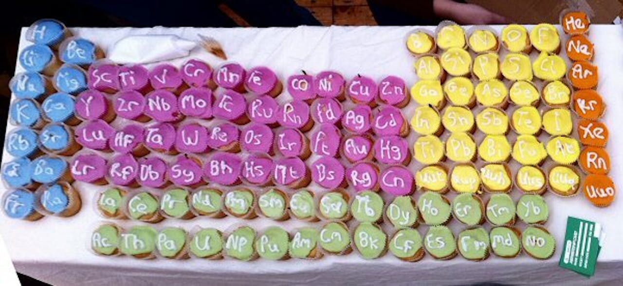 Een tafel vol met paarse, groene en gele cupcakes met elementen erop.