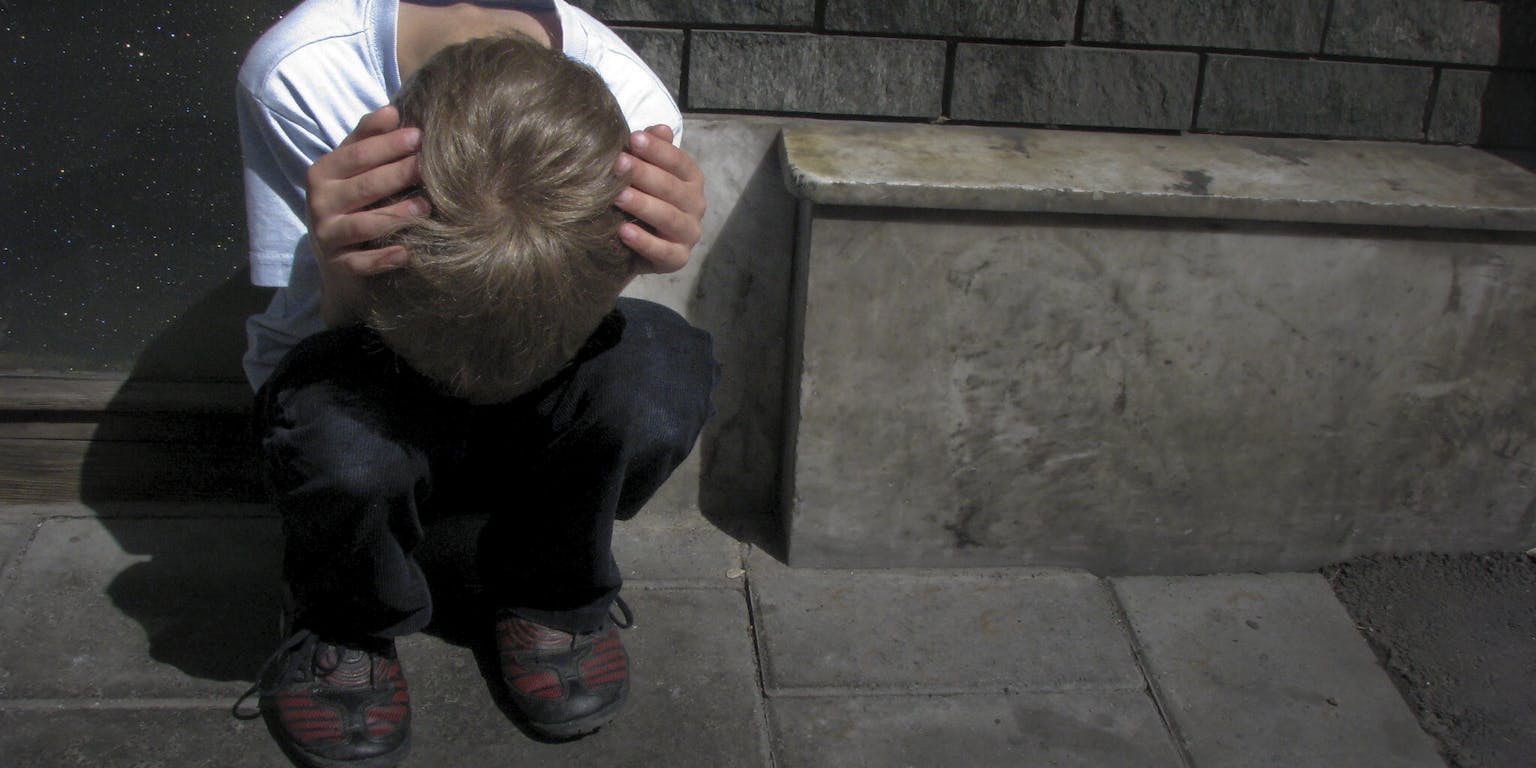 Een jongen zittend op de grond met zijn oren bedekt