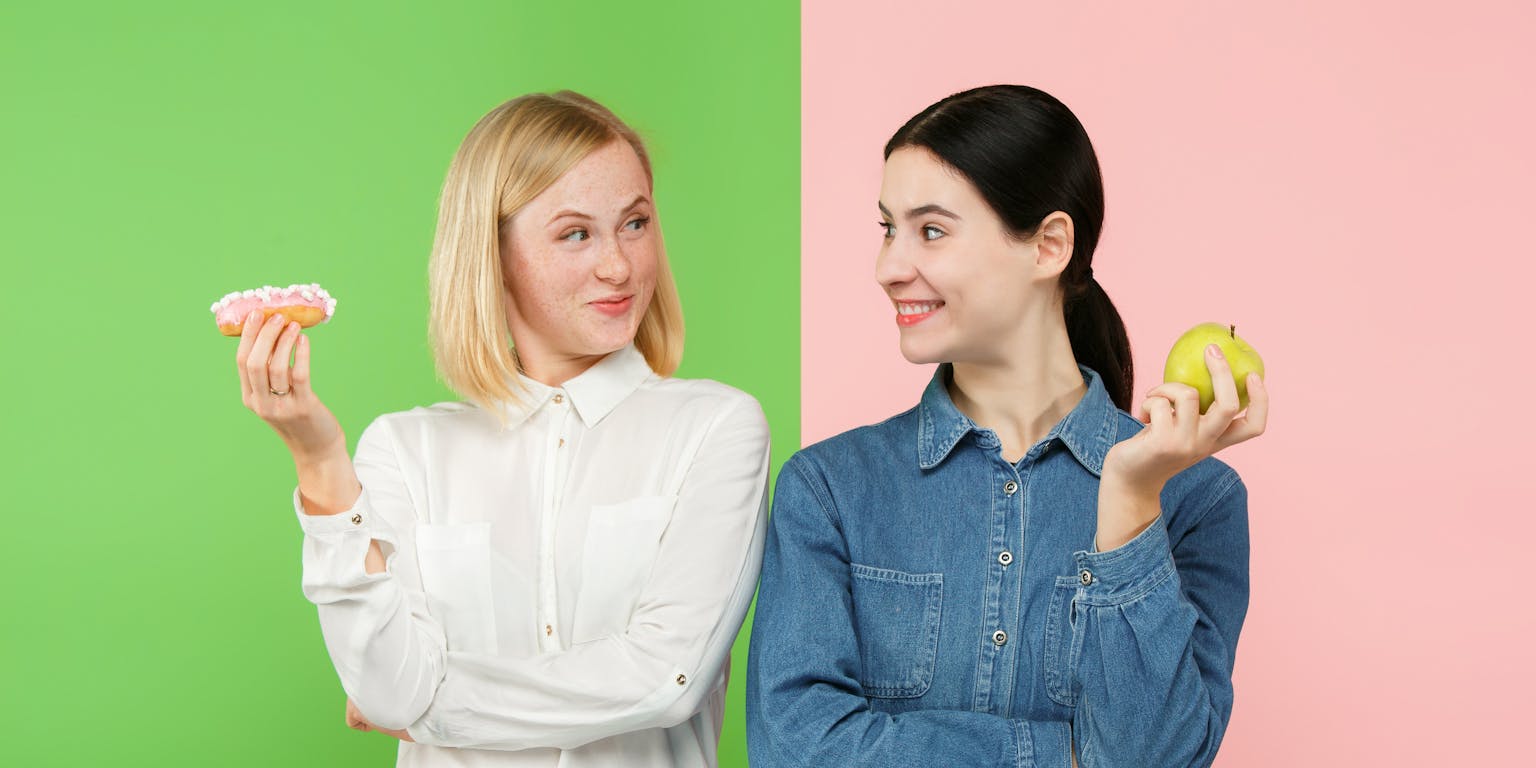 twee jonge vrouwen met een groene en roze achtergrond moeten kiezen tussen een gezonde appel eten, of een ongezond cakeje