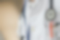 Een close-up van een doktersjas. Er is een stethoscoop te zien en een borstzakje vol met pennen.
