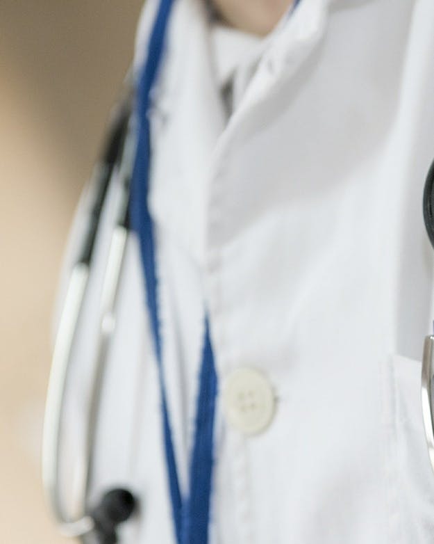 Een close-up van een doktersjas. Er is een stethoscoop te zien en een borstzakje vol met pennen.