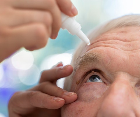 Oudere man krijgt oogdruppels toegediend door een zorgverlener