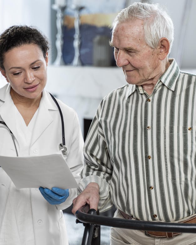Jonge vrouwelijke arts in witte doktersjas praat met oudere man achter een rollator Jonge vrouwelijke arts in witte doktersjas praat met oudere man achter een rollator