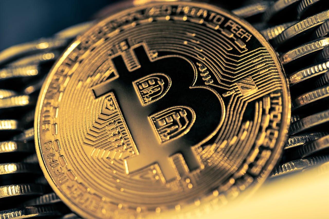 Een gouden munt met daarop het logo van Bitcoin staat rechtop tegen stapels van dezelfde munten.