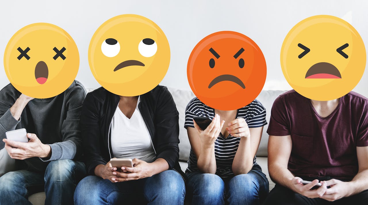 Vier mensen zitten naast elkaar met hun mobiel in hun hand. Over hun hoofden zijn grote emoji geplakt, die boos en verontwaardigd kijken.