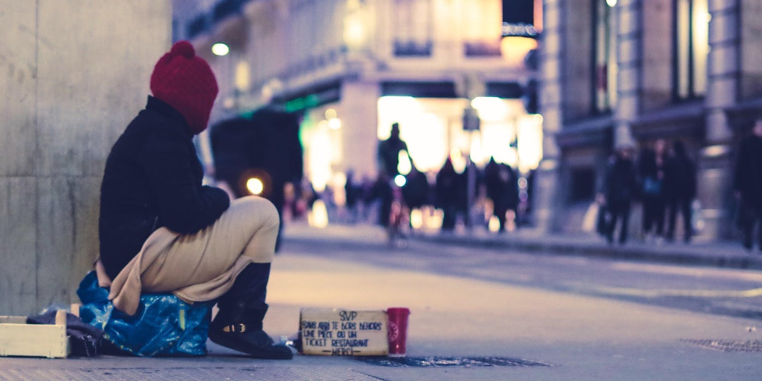 Een dakloze die op straat zit. Het is avond.