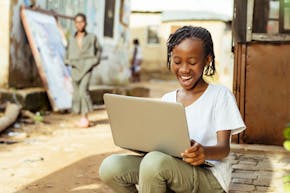 Enthousiast Afrikaans meisje zittend op de stoep met een laptop.