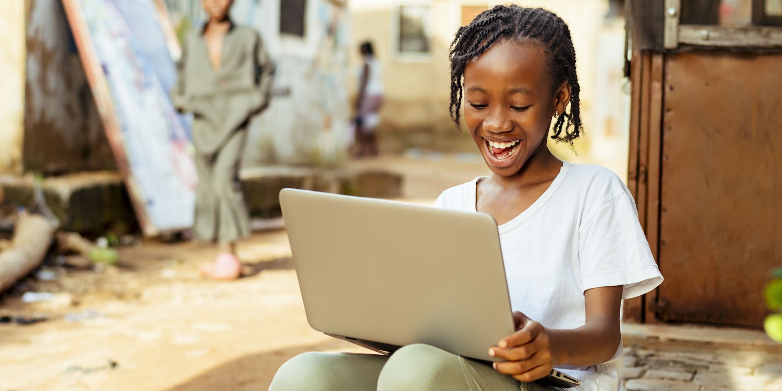 Enthousiast Afrikaans meisje zittend op de stoep met een laptop.
