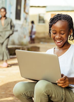 Enthousiast Afrikaans meisje zittend op de stoep met een laptop.