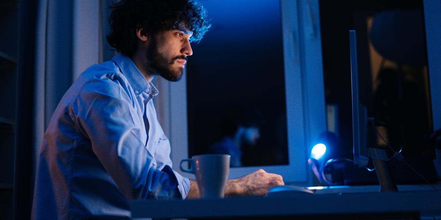 Een man zit in het donker te werken achter een computer.