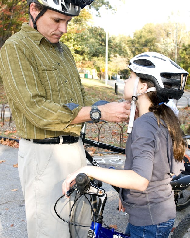 De meeste dodelijke slachtoffers in het verkeer zijn fietsers. Het (verplicht) dragen van een fietshelm zou veel van deze dodelijke verkeersongevallen kunnen voorkomen. Een vader met fietshelm, doet een fietshelm om bij zijn dochter