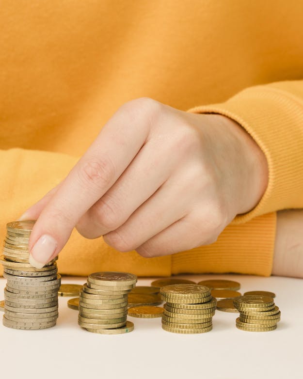 Investeer je zelf mee of profiteer je alleen van de totaalopbrengst? Armen van een vrouw leunend op een tafelblad met vier stapeltjes muntjes op tafel