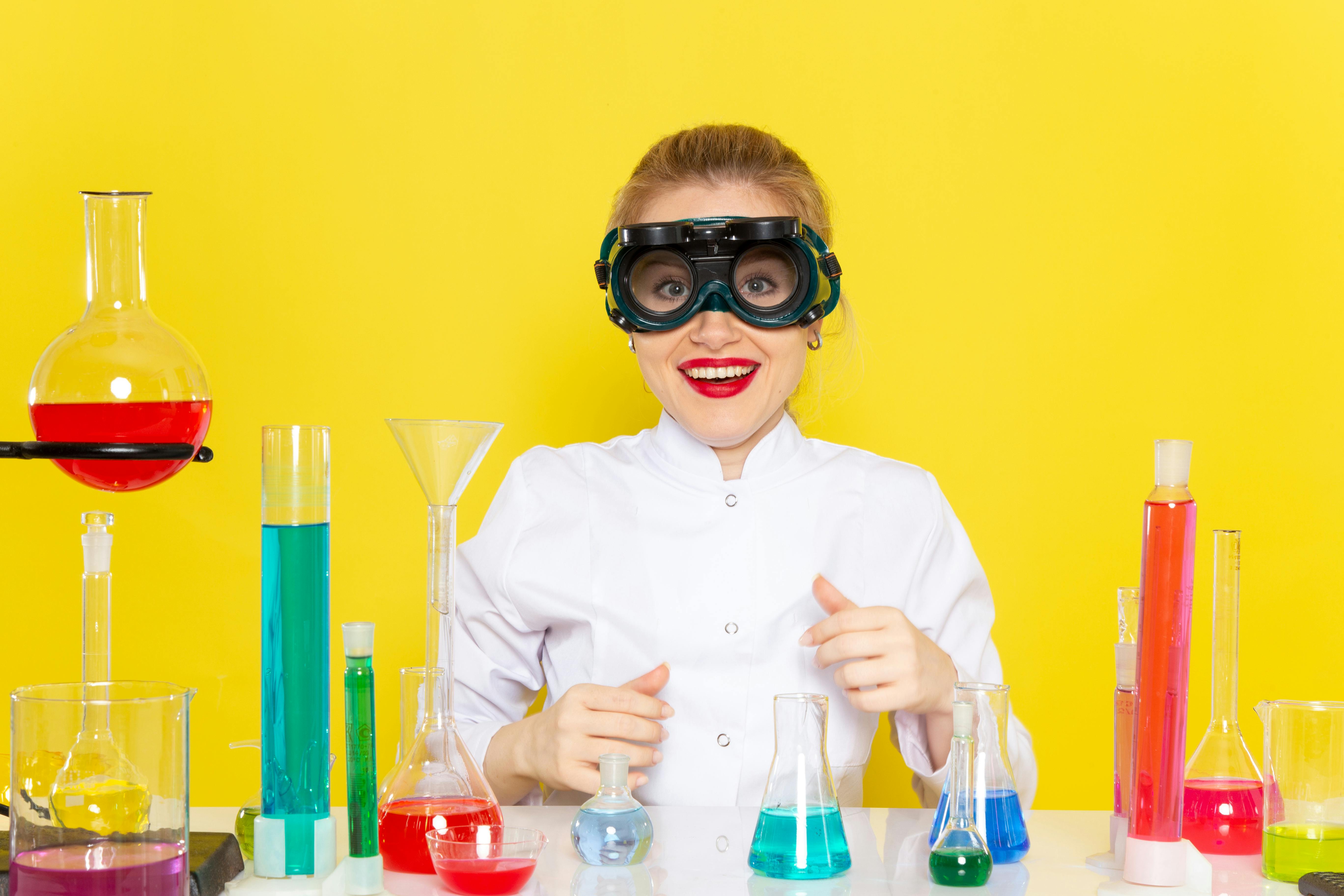 jonge vrouw met labjas aan en reageerbuisjes in allerlei kleuren