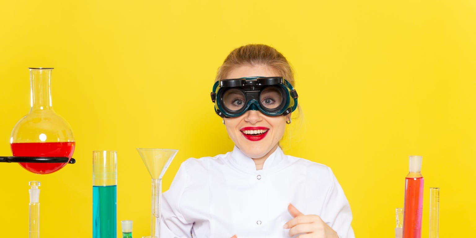 jonge vrouw met labjas aan en reageerbuisjes in allerlei kleuren