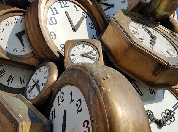 Een berg bruine, houten klokken, in verschillende formaten. Ze hebben wel allemaal een witte wijzerplaat en zwarte cijfers en wijzers.