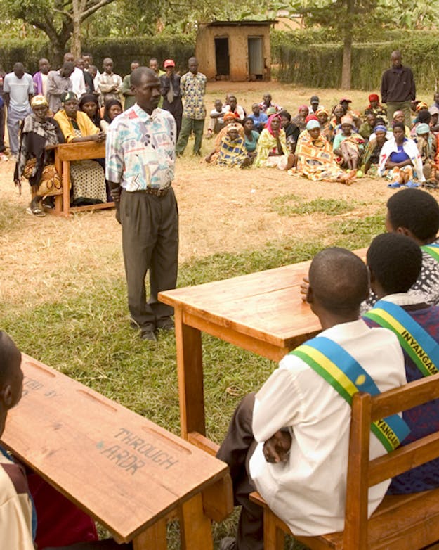 Gacaca court in Rwanda Traditionele rechtszaak in Rwanda. Man staat midden op een grasveld omringd door anderen.
