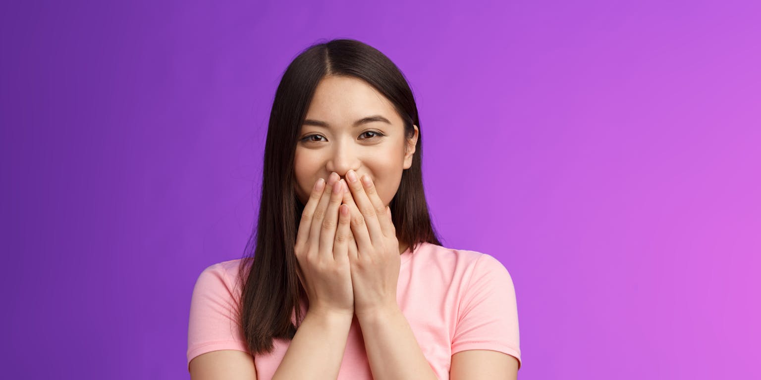 Een vrouw met donker haar bedekt haar glimlach met haar handen.