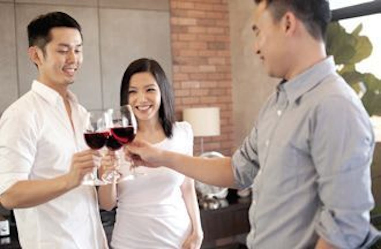 Drie personen proosten met elkaar met een glas rode wijn in hun hand.