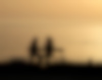 De silhouetten van twee mensen die bij zonsondergang een gesprek op een bankje voeren.