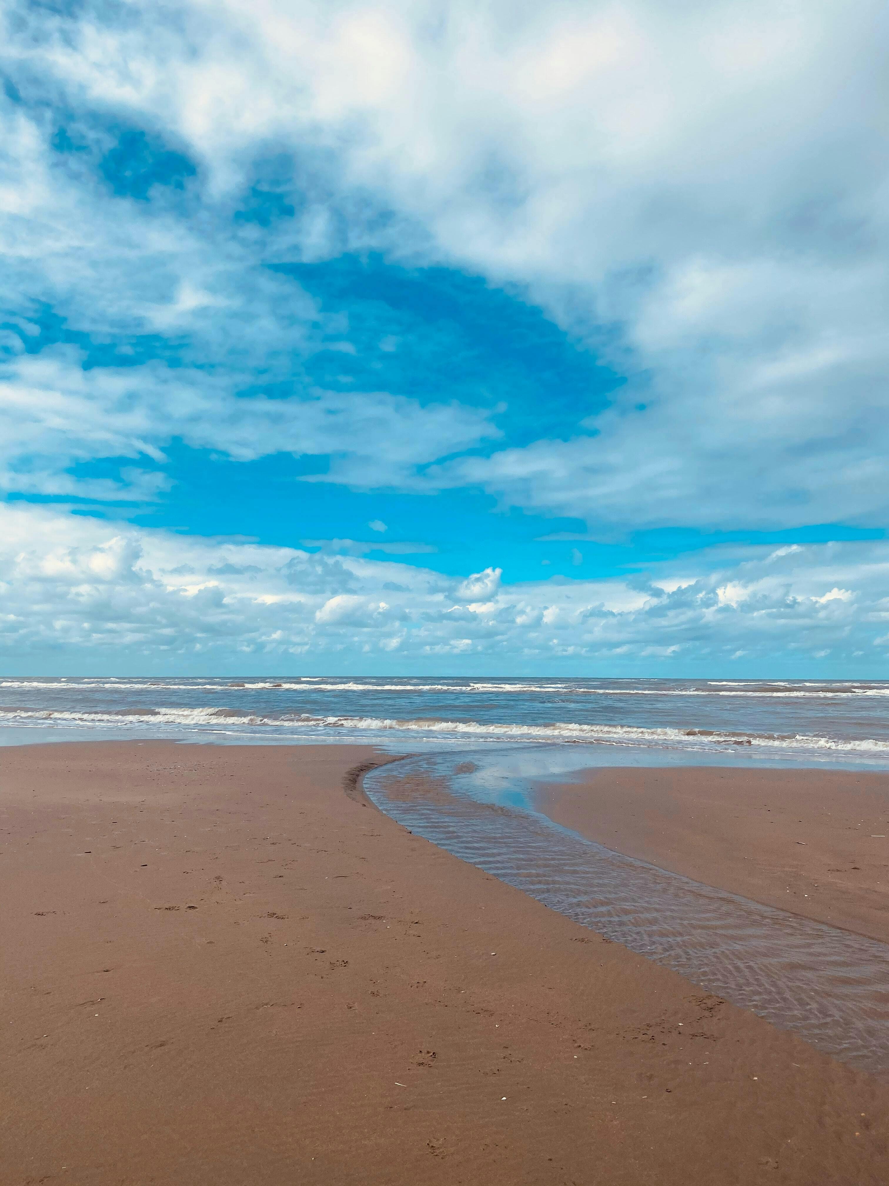 Een zandstrand met een blauwe lucht en wolken.