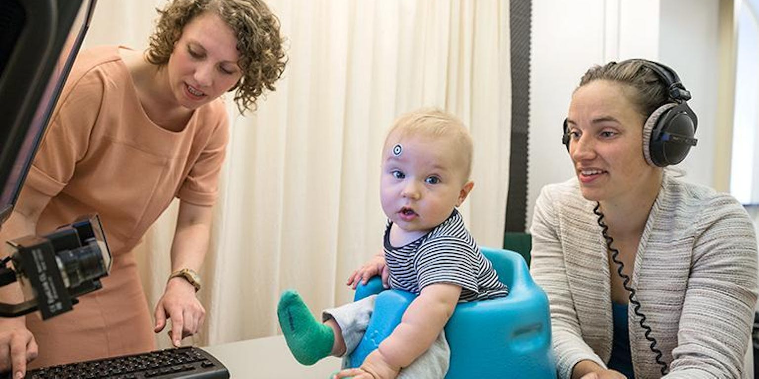 Een baby zit in een stoel terwijl een vrouw op een computer werkt.