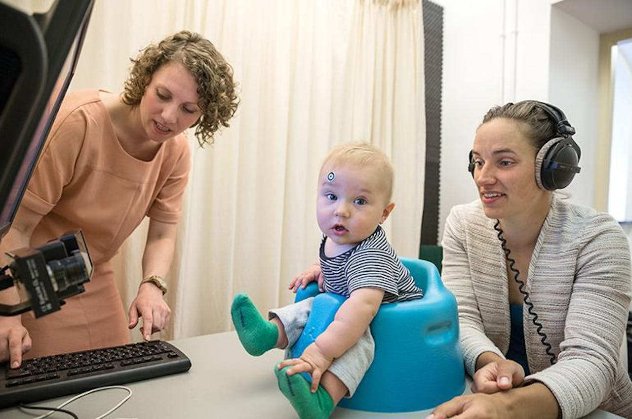 Een baby zit in een stoel terwijl een vrouw op een computer werkt.