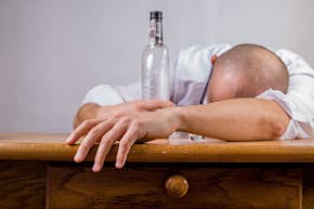 Een man slaapt op tafel met een fles alcohol in zijn hand.