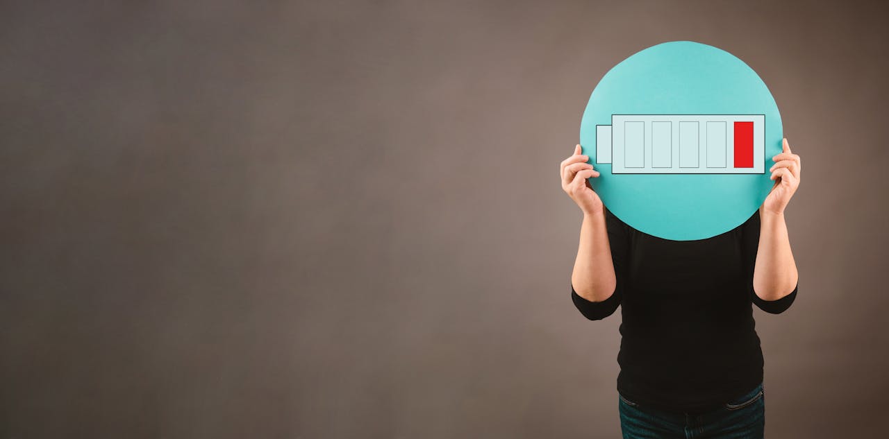 Door veel stress en verantwoordelijkheden tegelijk kan je batterij leegraken. lege batterij uitgeknipt die iemand voor zijn gezicht houdt