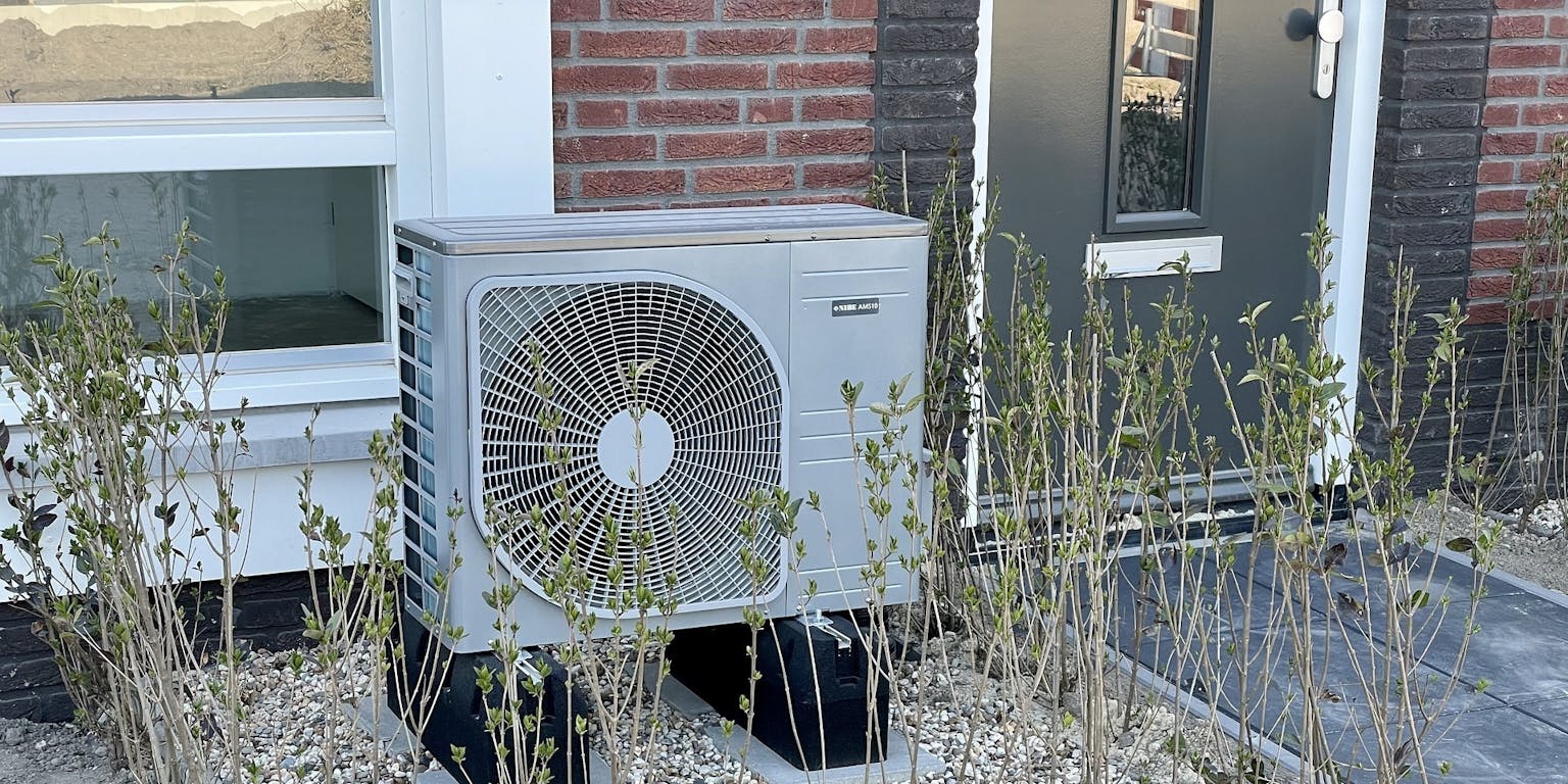 In de voortuin van een huis staat een airconditioning unit.