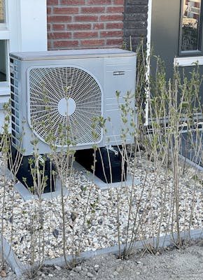 In de voortuin van een huis staat een airconditioning unit.
