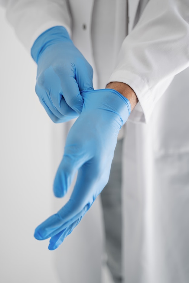 Een arts in een witte doktersjas trekt blauwe rubberen handschoenen aan.