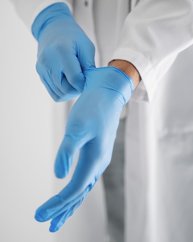 Een arts in een witte doktersjas trekt blauwe rubberen handschoenen aan.