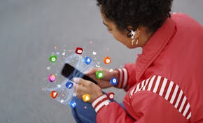 Een jongedame in een rode jas kijkt naar haar telefoon met oordopjes in. De camera kijkt over haar schouder. Rond de telefoon zweven icoontjes van verschillende apps.