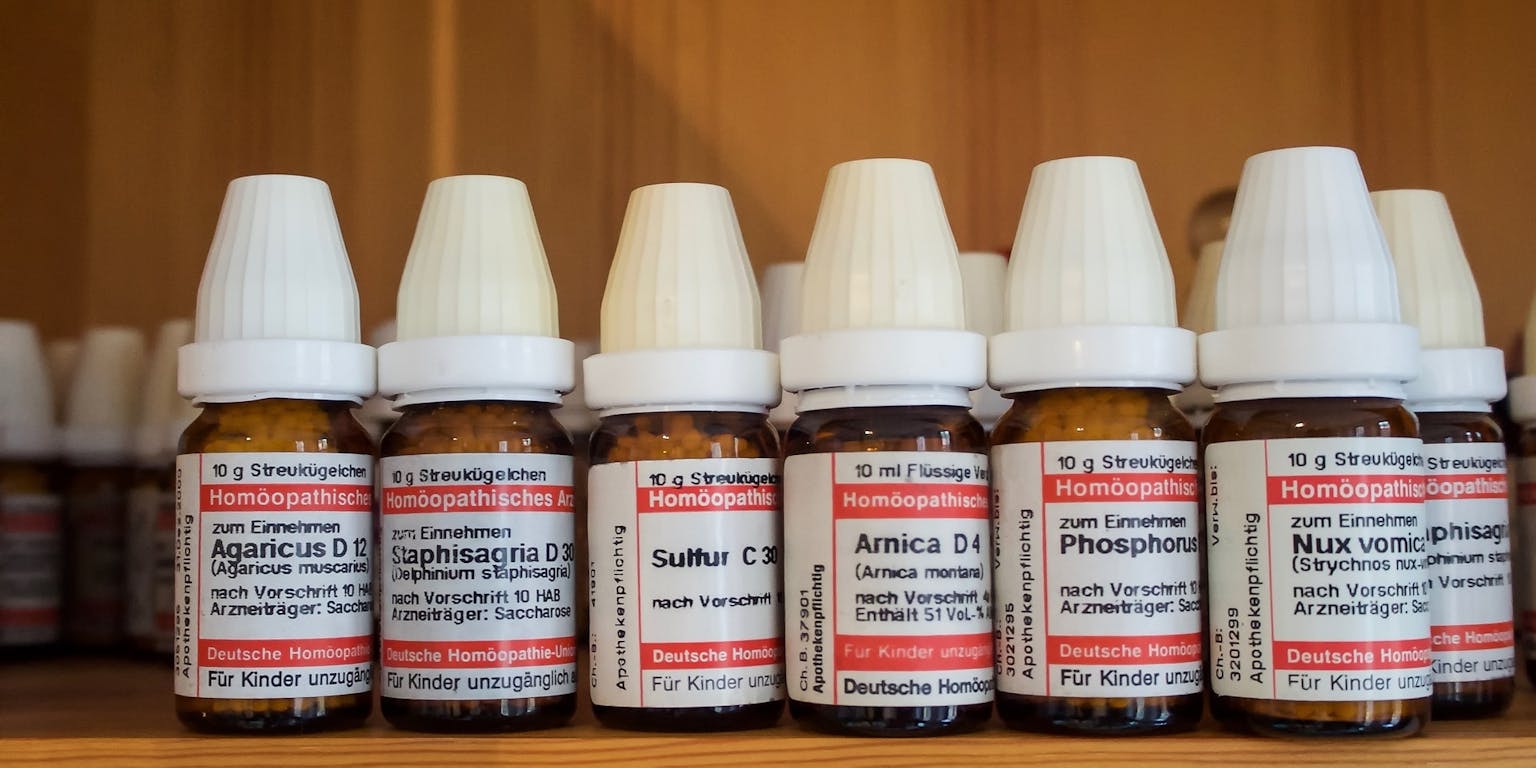 Een plank met een rij flesjes, gevuld met verschillende homeopatische middelen.