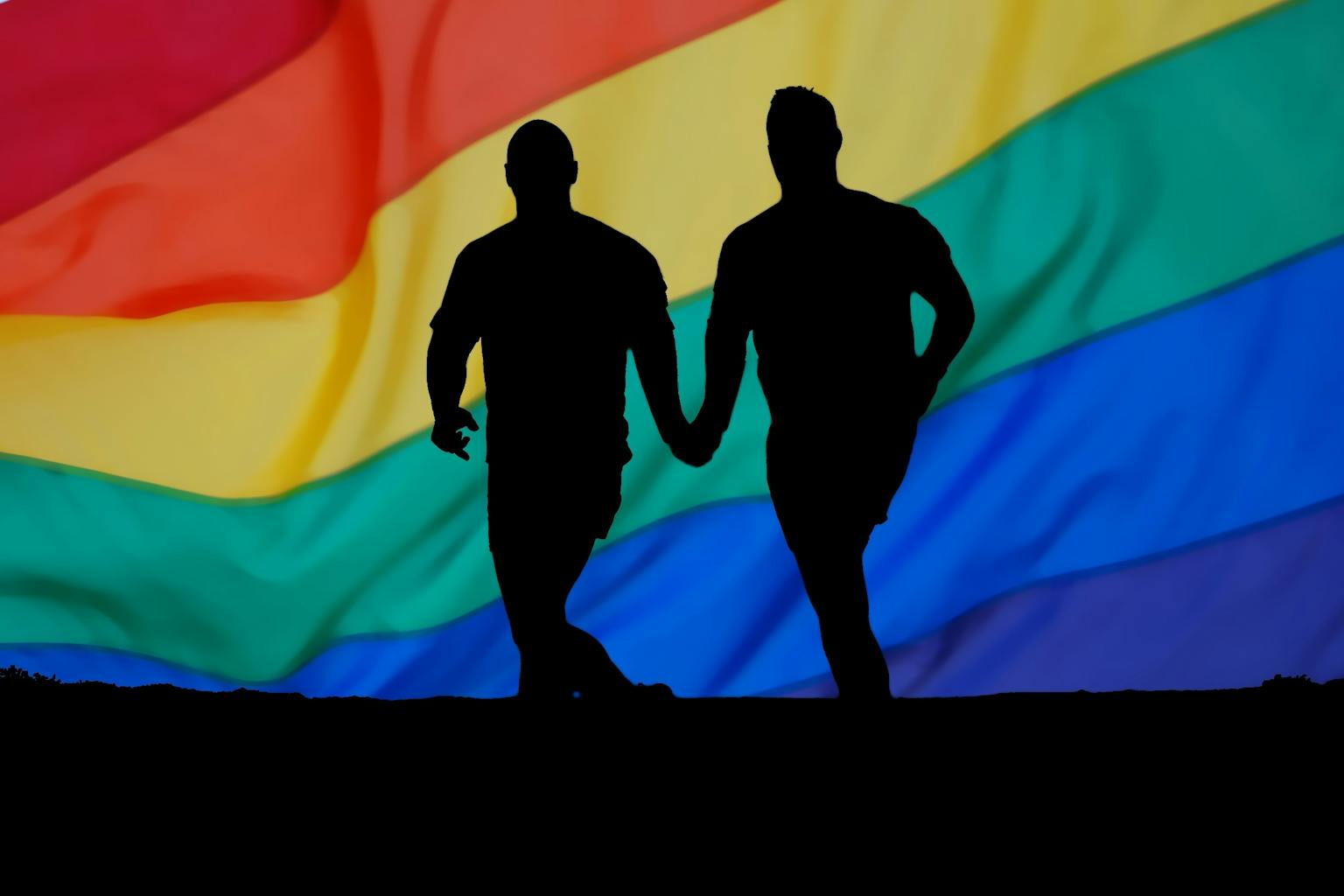 Twee mensen hand in hand voor een regenboogvlag.
