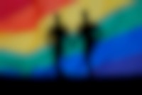 Twee mensen hand in hand voor een regenboogvlag.