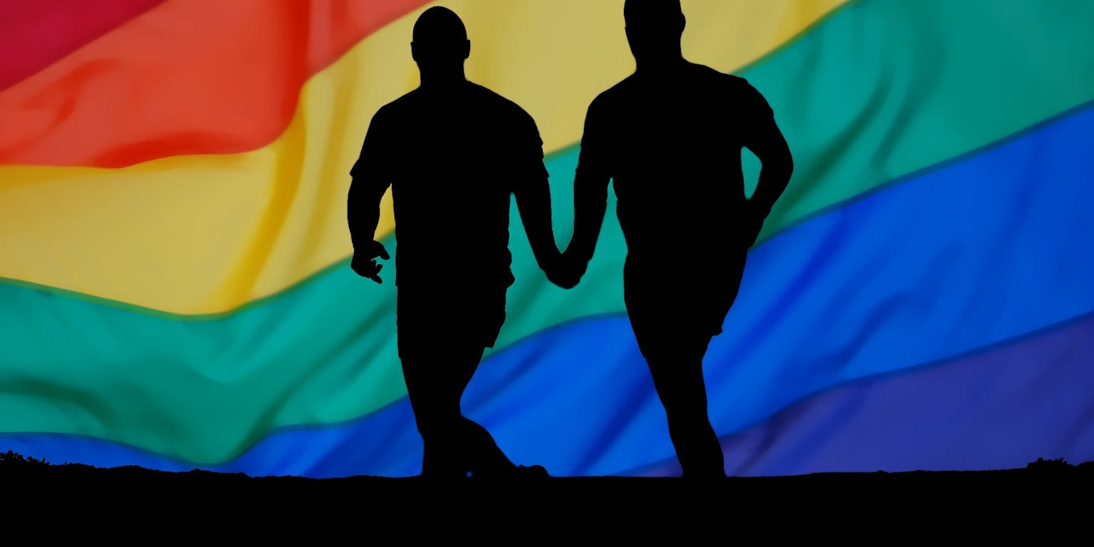 Twee mensen hand in hand voor een regenboogvlag.